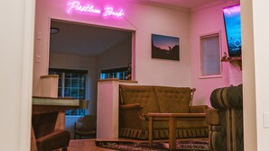 Ein Wohnzimmer mit Holzboden, einer Couch, einem Couchtisch und einem Neonlichtschild mit der Aufschrift 'Poet's Bench'.
