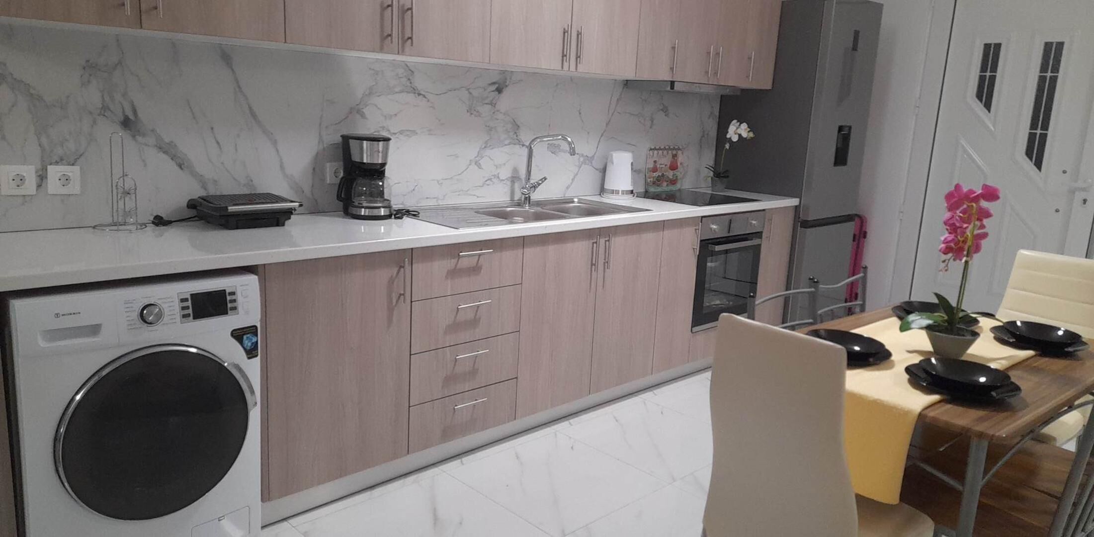 Una cocina moderna con lavadora integrada, cafetera y lavamanos.