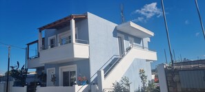 A two-story residential building with a balcony on the upper floor, a small attached structure with a balcony, and a staircase leading to the upper level. - Gennadi Retreat - House 2 (Rhodes)