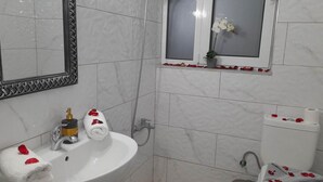 A bathroom with a white sink, a mirror with a decorative frame, a toilet, and a window with a potted orchid. - Gennadi Retreat - House 2 (Rhodes)
