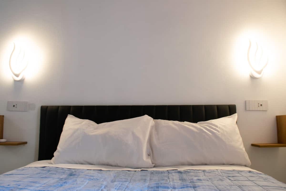 A bed with white pillows and a blue quilt, flanked by two wall-mounted light fixtures.