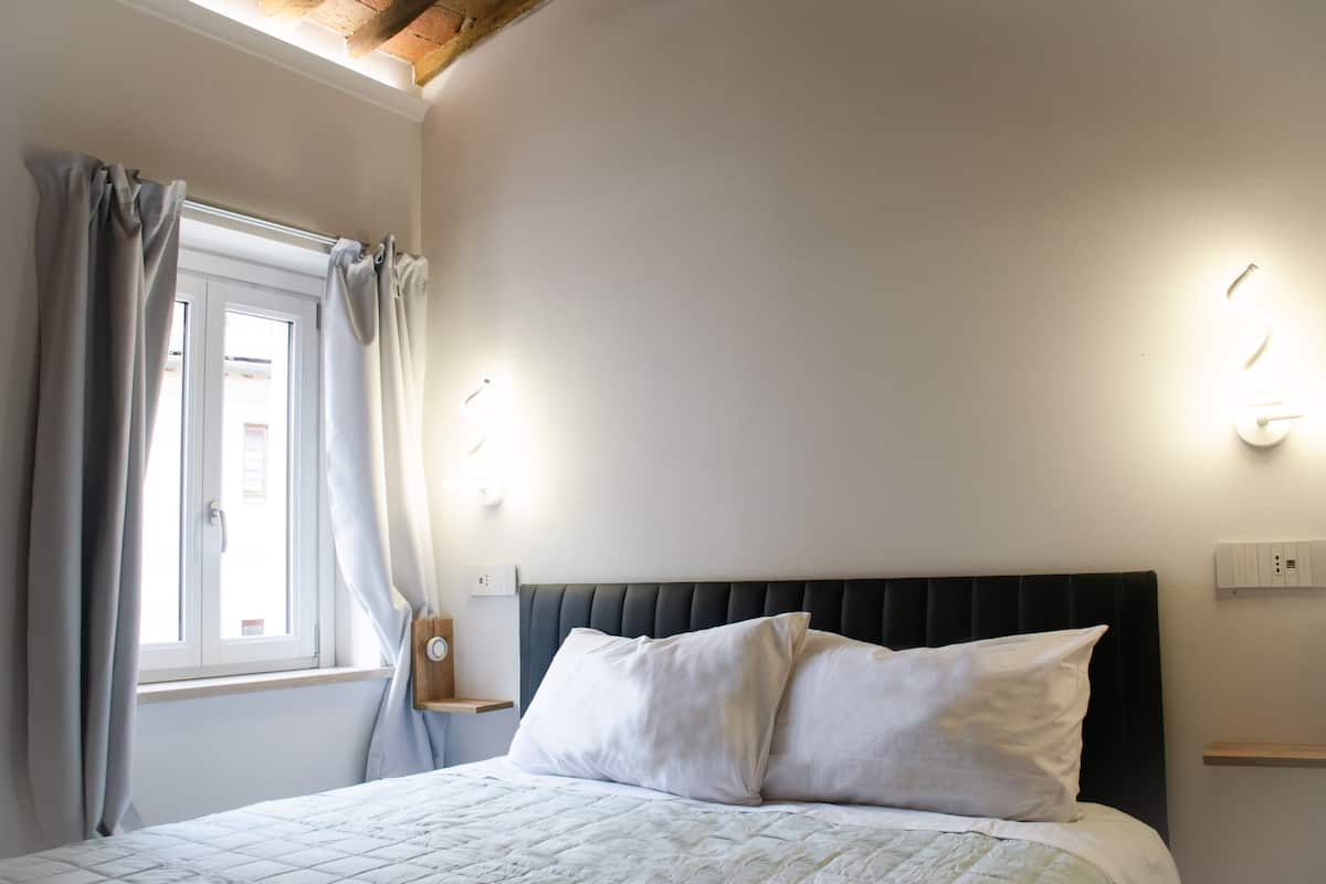 A bedroom with a bed, curtains, a window, and wall-mounted lights.