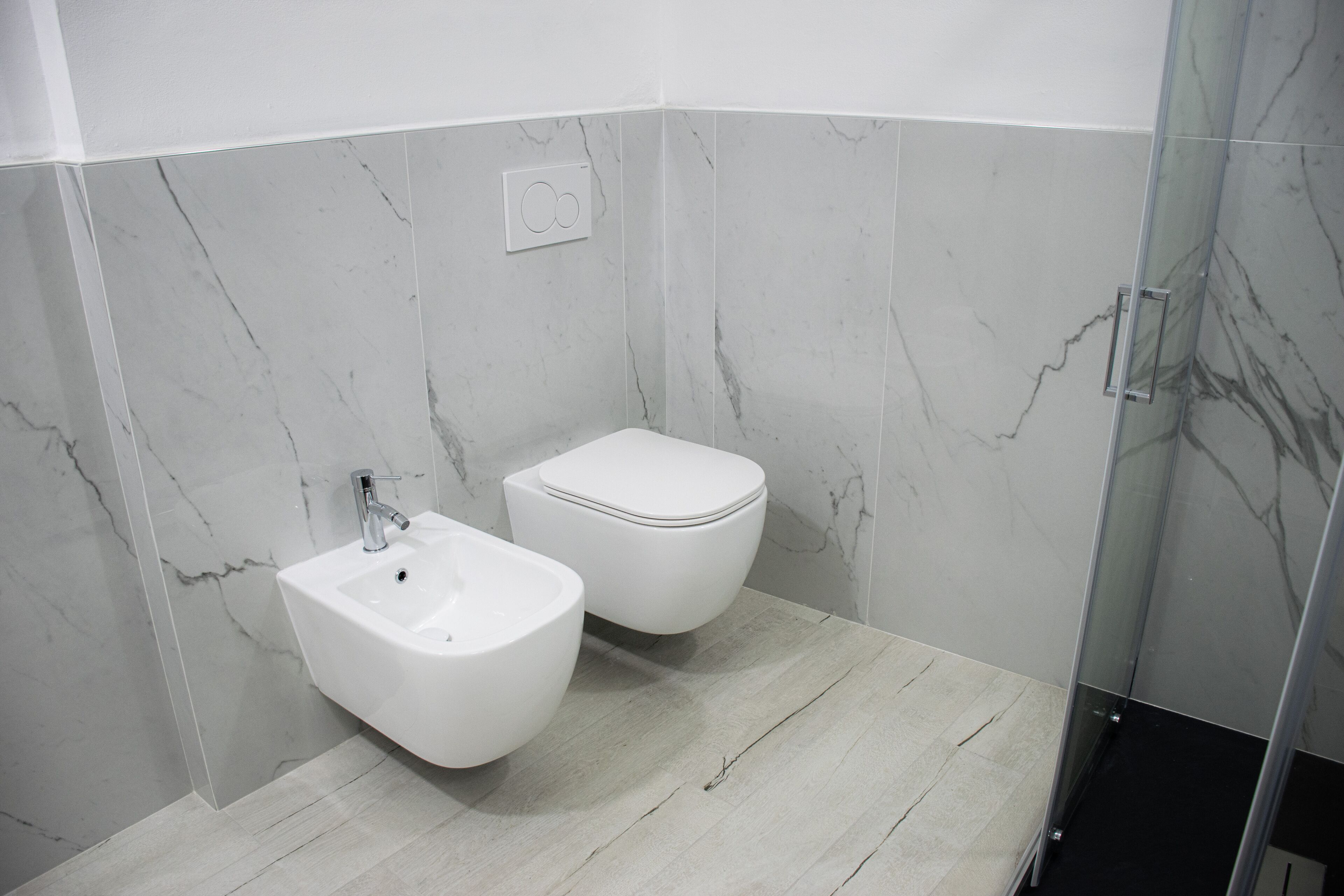 A modern bathroom with a marble wall, a white sink, and a toilet.