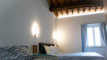 A bedroom with two beds, a wooden ceiling, a window with curtains, and a wall-mounted light.