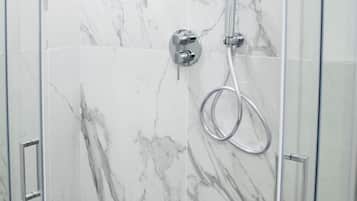Une douche fermée par des parois de verre, avec un mur en marbre, une douchette à main et un panneau de commande.