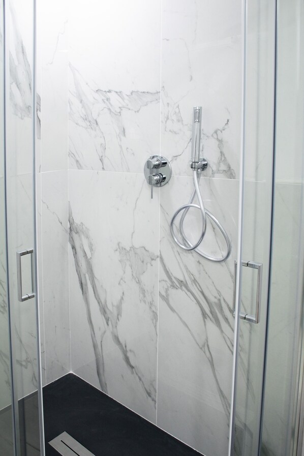 A glass-enclosed shower with a marble wall, a handheld showerhead, and a control panel. - Room Rent Morrona (Terricciola)