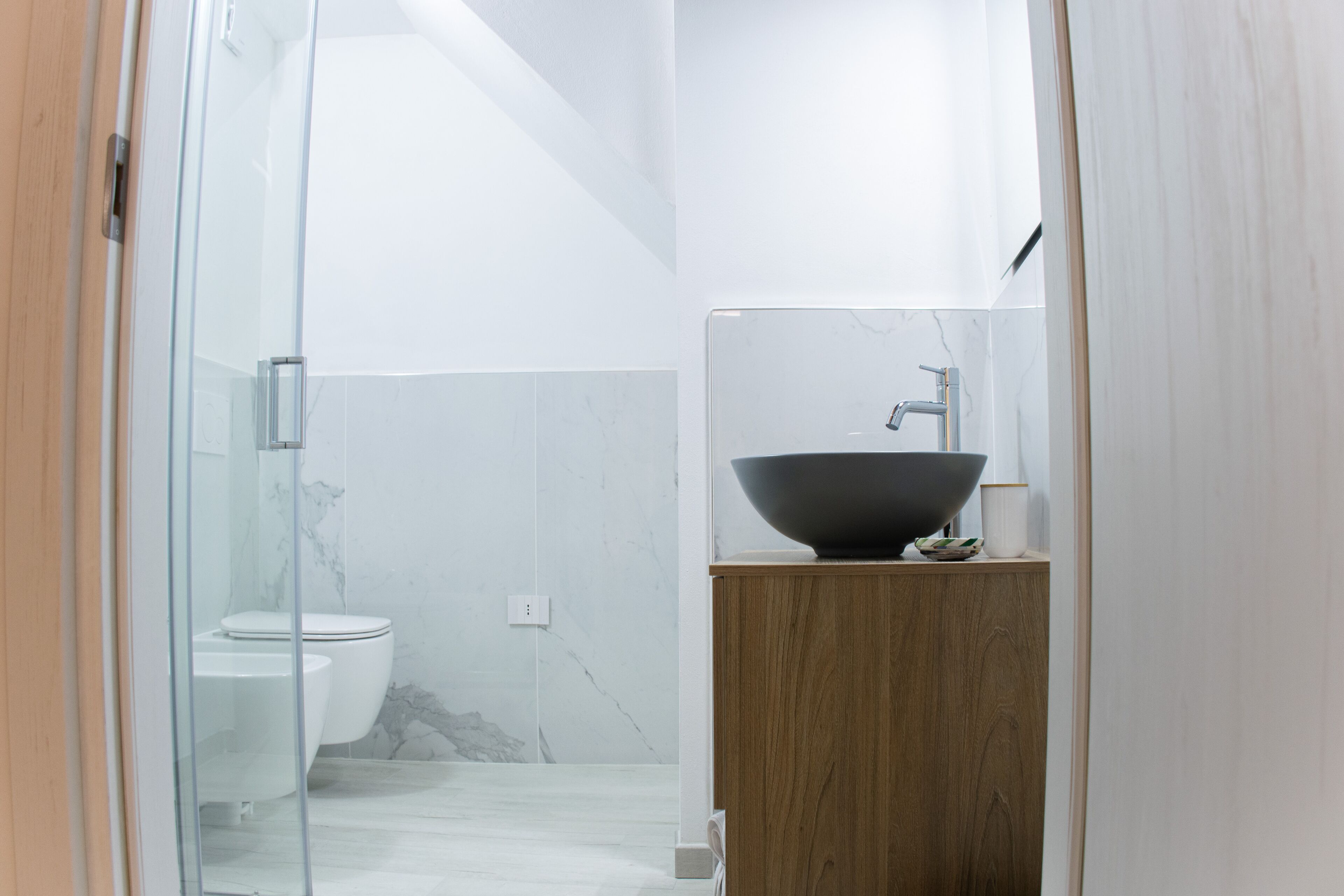 A modern bathroom with a glass shower enclosure, a white toilet, and a wooden vanity with a large black basin.