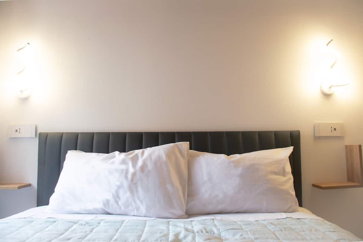 A bed with a headboard, two bedside tables, and wall-mounted lights.