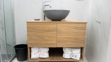 A modern bathroom with a wooden vanity, a large vessel sink, and marble walls.