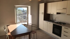 Une cuisine compacte avec un coin repas, une fenêtre donnant sur des immeubles et des arbres, et un plafond en bois.