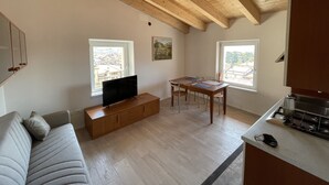 Un salon moderne avec un plafond en bois, un téléviseur à écran plat, un canapé, une table à manger avec des chaises et un coin cuisine équipé d’une cuisinière.