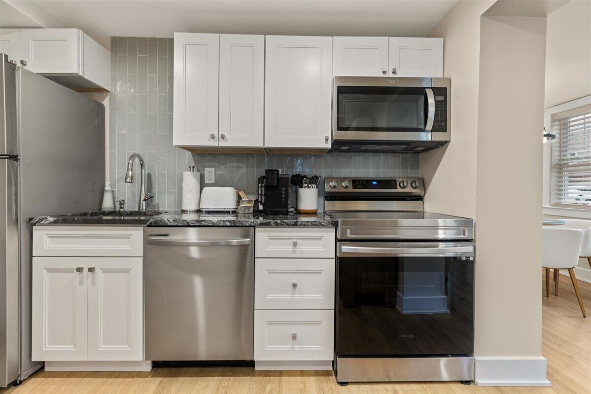 A modern kitchen with white cabinets, stainless steel appliances, and a black oven.