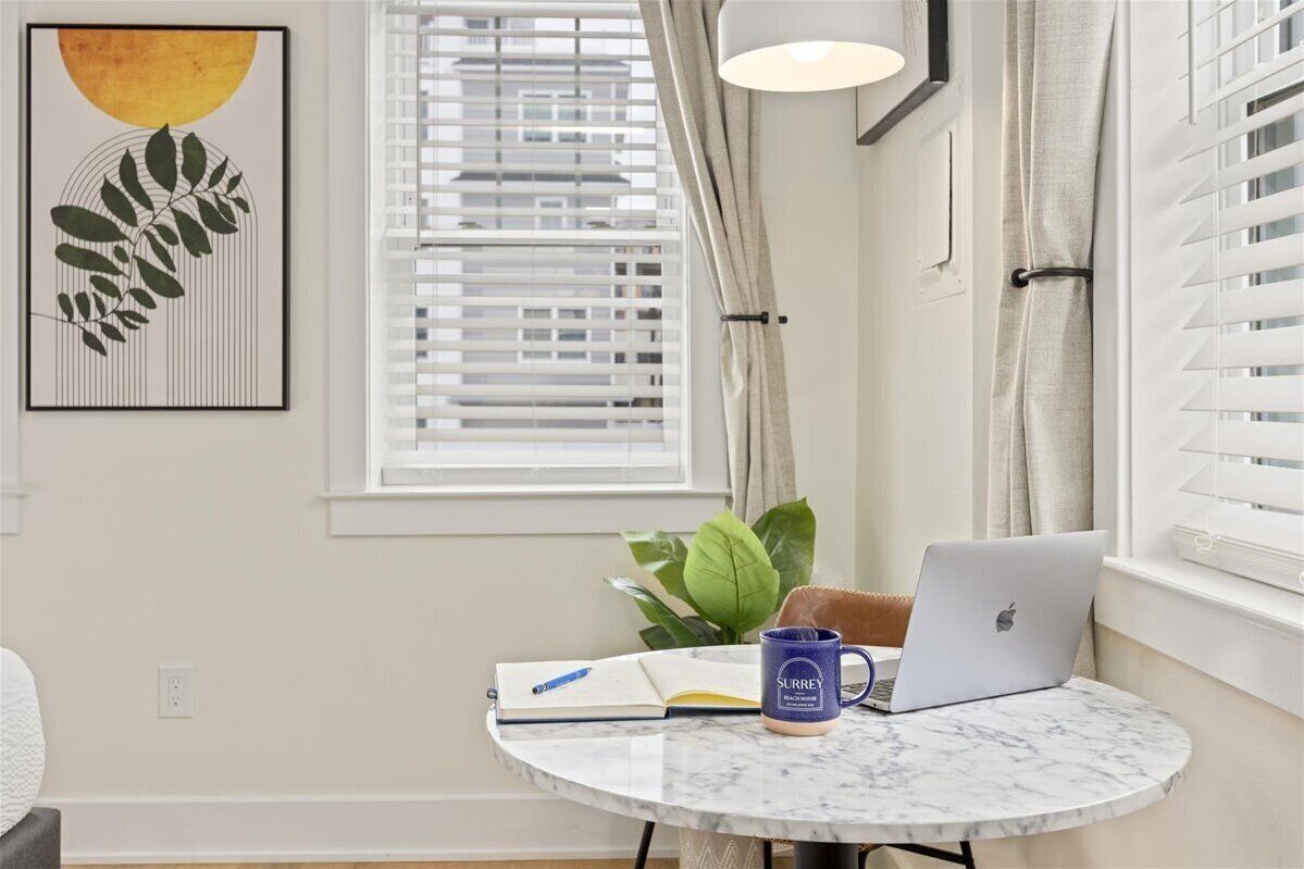 A room with a round marble table, a laptop, a notebook, a pen, and a mug.
