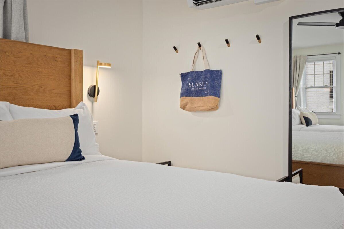 Habitación de hotel con cabecera de madera, cama con ropa blanca, lámpara de pared y un bolso colgado con texto.