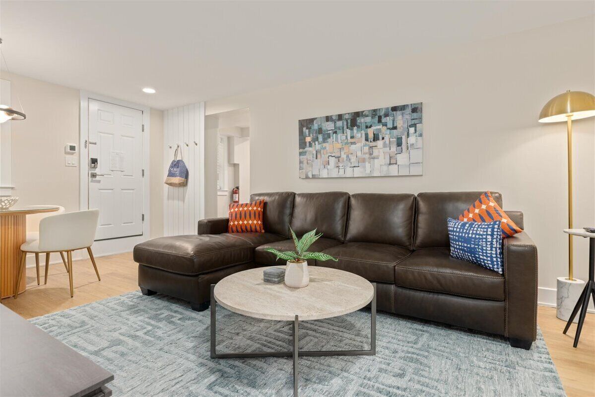 A living room with a brown leather sofa, a round coffee table, and a painting on the wall.