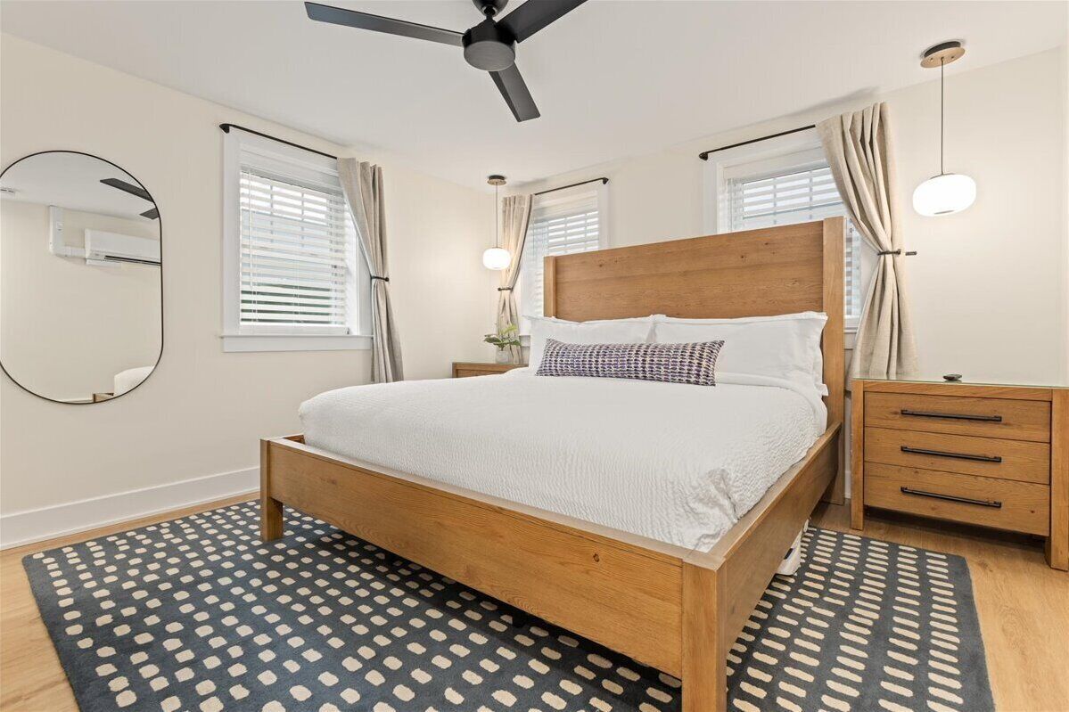 A bedroom with a wooden bed, a ceiling fan, a bedside table, and a mirror.