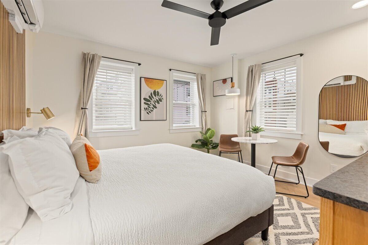 A hotel room with a large bed, two chairs, a small table, and a ceiling fan.