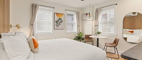 A hotel room with a large bed, two chairs, a small table, and a ceiling fan.