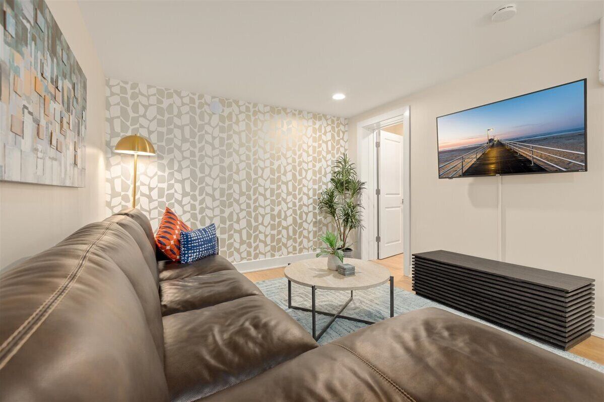 Ein Wohnzimmer mit einem braunen Ledersofa, einem runden Couchtisch, einem Blumentopf und einem Fernseher an der Wand.