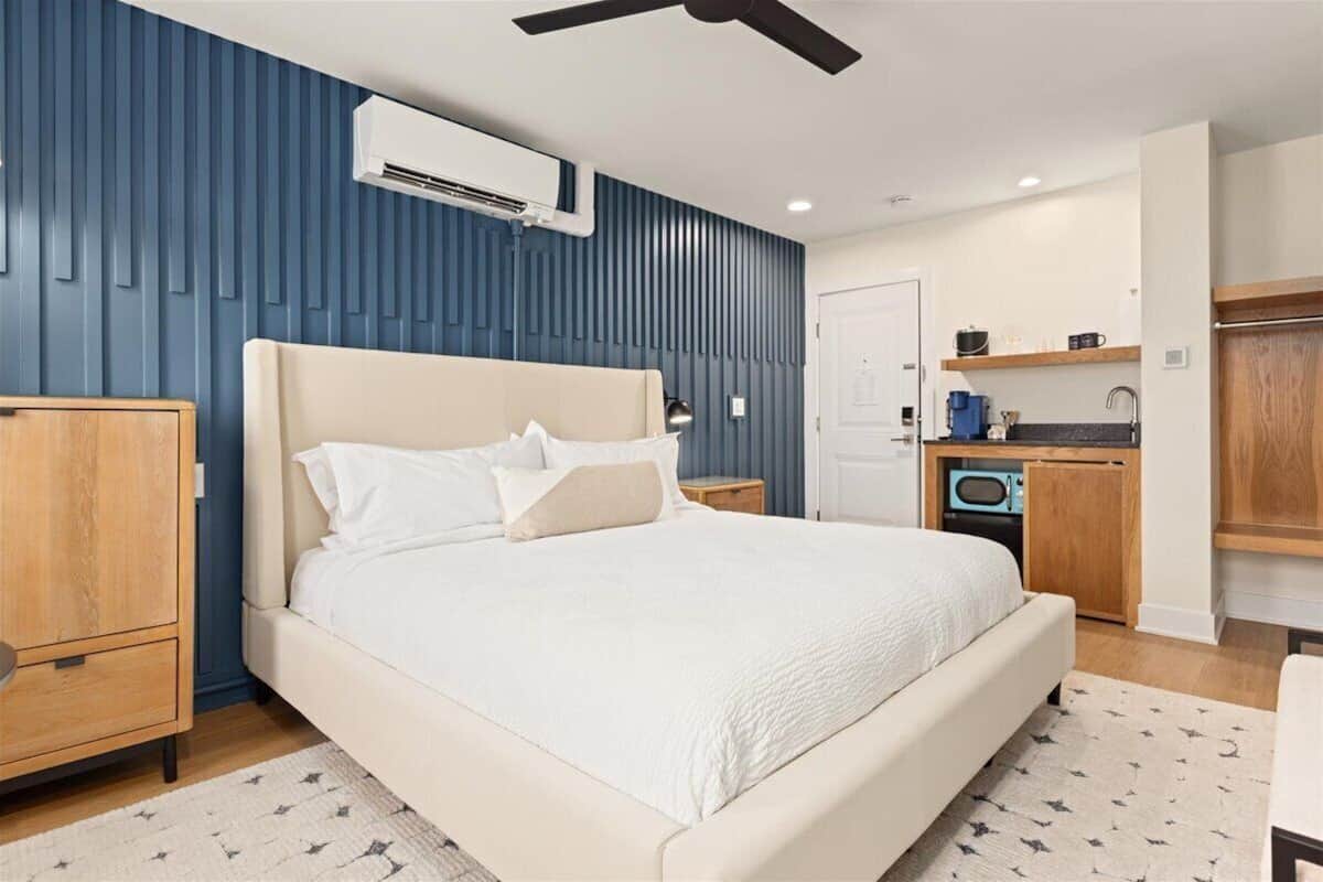 A bedroom with a bed, bedside tables, a wardrobe, a built-in kitchen area, and a ceiling fan.