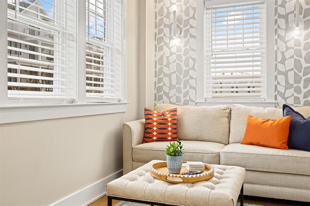 A living room with a beige sofa, a coffee table with a tray, and patterned wallpaper.