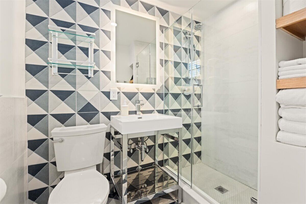 A bathroom with a geometric tile pattern, a glass shower enclosure, a white sink, and a towel rack.