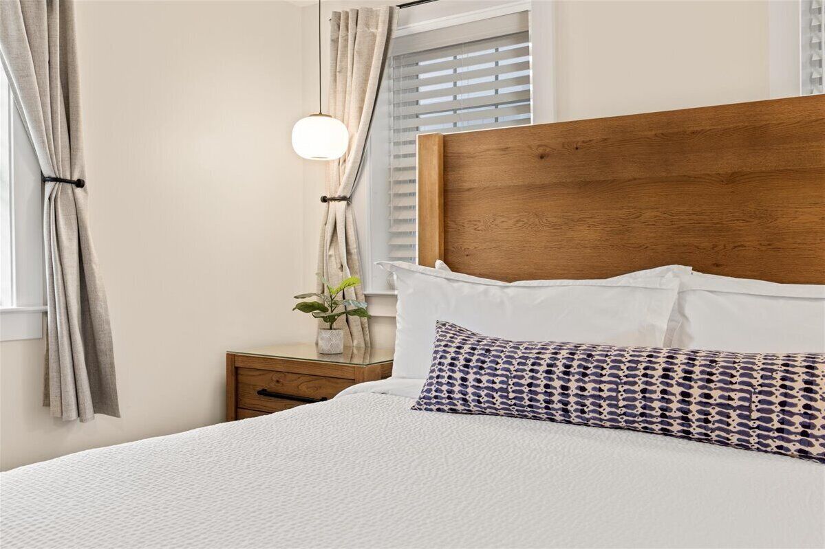 A neatly made bed with a wooden headboard, white bedding, and a patterned pillow.