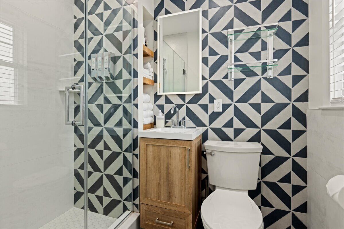 A bathroom with a geometric tile pattern, a wooden cabinet, a glass shower enclosure, and a white toilet.