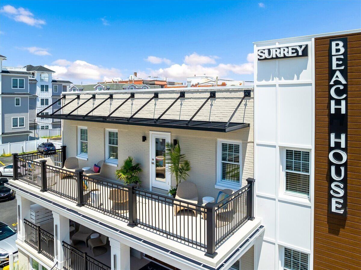 Un edificio de dos pisos con un balcón, un letrero que dice "SURREY BEACH HOUSE" y vistas del vecindario circundante.