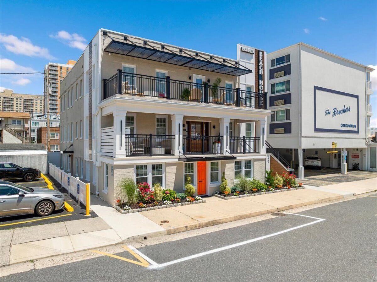 A multi-story hotel with balconies, a red door, and a parking area with cars.