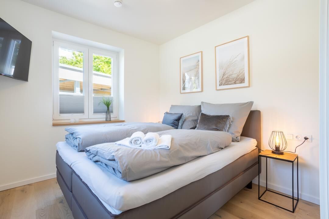 Ein modernes Schlafzimmer mit einem großen Bett, einem Nachttisch mit Lampe und zwei gerahmten Bildern an der Wand.