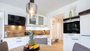 A modern kitchen with white cabinets, a wooden countertop, and a black stove. There is a fruit bowl on the dining table. - Villa Dornkamp - Apartment 1 - Vacation in style. Close to the beach. Modern. Central. (Timmendorfer Strand)