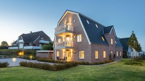 A modern two-story house with a balcony, a well-maintained lawn, and a small pond. - Villa Dornkamp - Apartment 1 - Vacation in style. Close to the beach. Modern. Central. (Timmendorfer Strand)