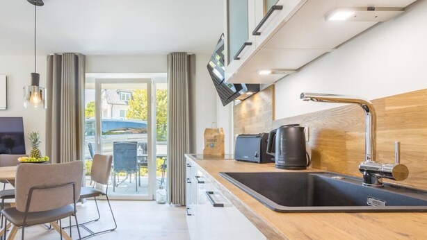A modern kitchen with a large sink, a coffee maker, and a toaster. There is a dining area with chairs and a table visible through a glass door. - Villa Dornkamp - Apartment 1 - Vacation in style. Close to the beach. Modern. Central. (Timmendorfer Strand)