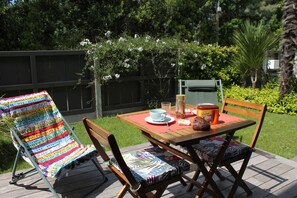 Eine Holzterrasse mit einem Tisch für zwei Personen, einem farbenfrohen Streifenstuhl und einem Holzstuhl mit gemustertem Kissen.