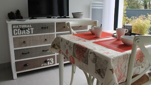 A dining area with a table set for two, a television on a cabinet, and a view of the outdoors. - CLASS 3* STUDIO 1 MINUTE FROM THE BEACH (Andernos-les-Bains)