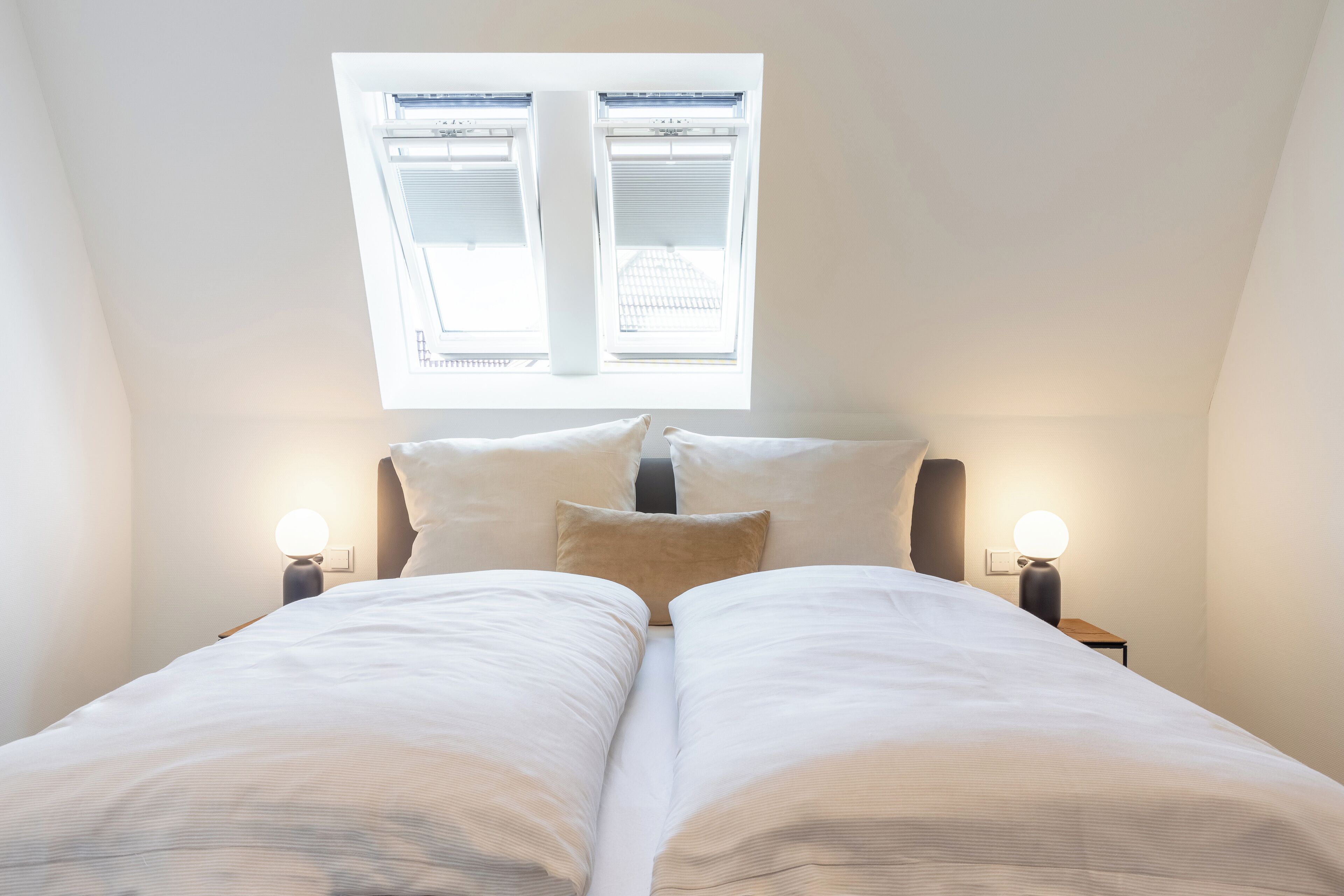 Een slaapkamer met een dakraam, twee nachtkastjes met lampen, en een bed met wit beddengoed.