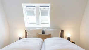 A bedroom with a skylight, two bedside tables with lamps, and a bed with white bedding.