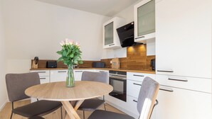 A modern kitchen with a round wooden table, grey chairs, a vase with flowers, and white cabinets.