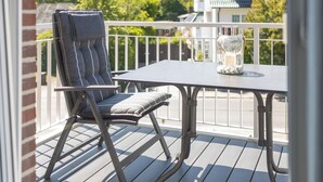A balcony with a table and a chair, a glass jar with stones, and a view of a house and trees.