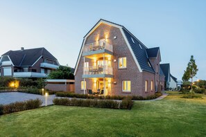 A modern two-story house with a balcony, a well-maintained lawn, and a driveway.