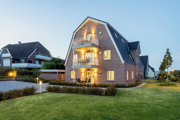 A modern two-story house with a balcony, a well-maintained lawn, and a driveway.