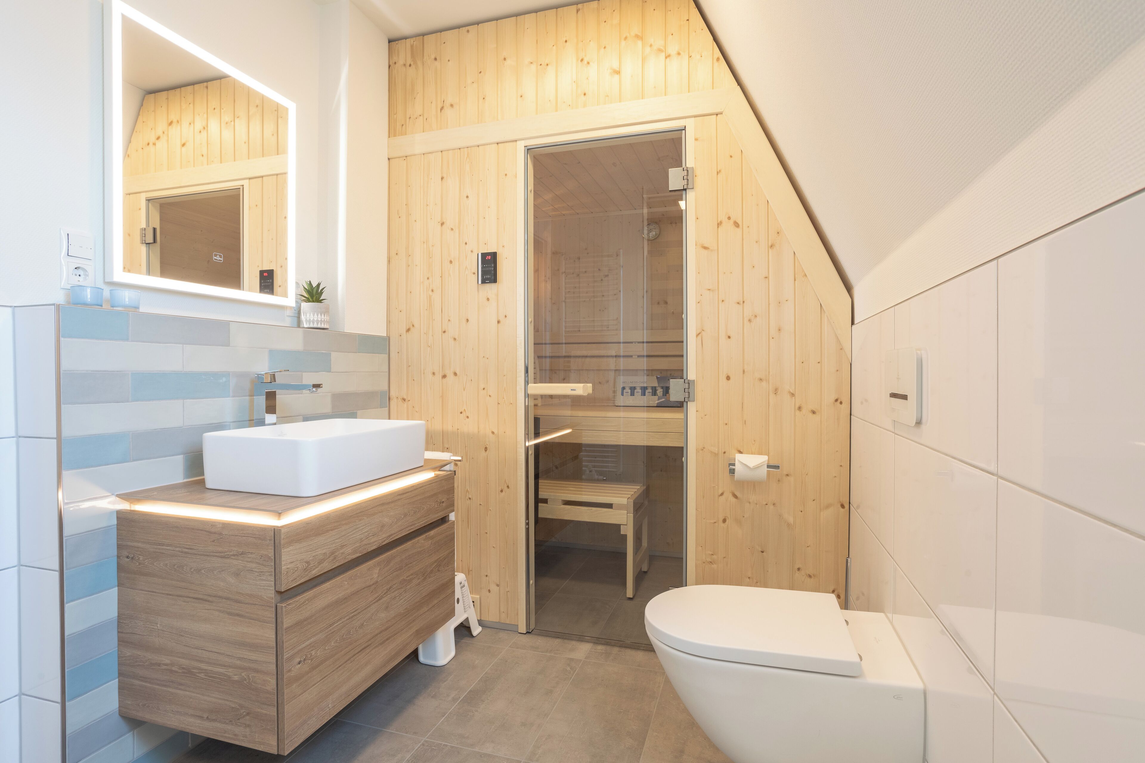 Un baño moderno con un tocador de madera, un lavamanos blanco y una ducha con cerramiento de vidrio.