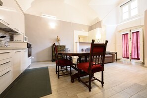 A modern kitchen with built-in appliances, a dining area with a wooden table and chairs, and a large window with curtains.
