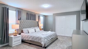 A bedroom with a large bed, two bedside tables, a wardrobe, and a television on the wall. - Avengers Game Room • Themed Rooms • South-Facing Pool & Spa • Near Disney (Kissimmee)