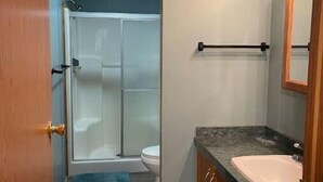 A bathroom with a shower, toilet, sink, and wooden cabinets. - Woof pack shack #1 (West Leyden)
