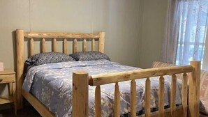 A wooden bed with a headboard, a ceiling fan, and a window with curtains. - Woof pack shack #1 (West Leyden)