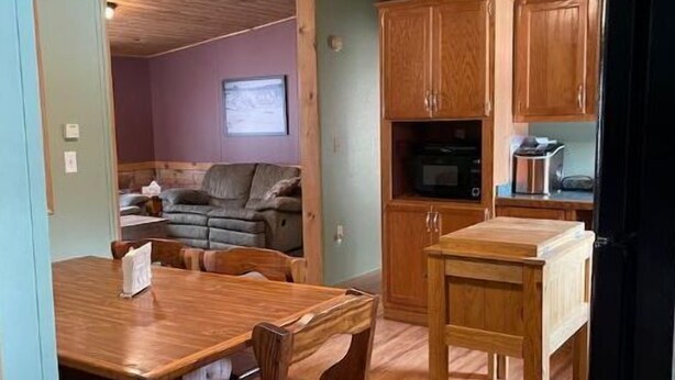 A wooden dining table with chairs, a kitchen area with wooden cabinets and appliances, and a living room with a couch and a television. - Woof pack shack #1 (West Leyden)