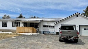 A single-story building with a garage, a wooden deck, and a parked Jeep. - Woof pack shack #1 (West Leyden)
