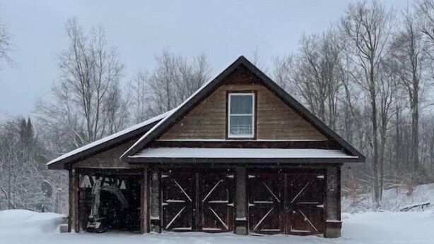 A wooden cabin with a garage, surrounded by snow-covered ground and trees. - Woofpackshack #4 (West Leyden)
